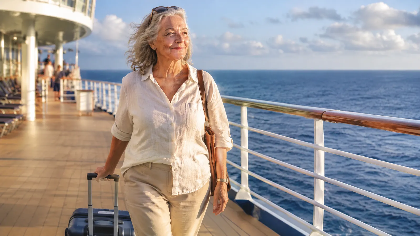 An older woman rolling a carry-on suitcase along a cruise ship deck